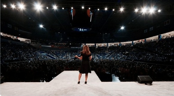 Summit delegate speaking on the main stage to a packed arena